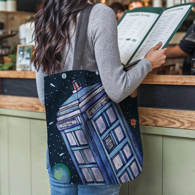 Police call box floating in the solar system tote bag hanging on the shoulder of a woman at a restaurant counter.